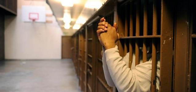 Image of inmate with hands outside of bars of cell